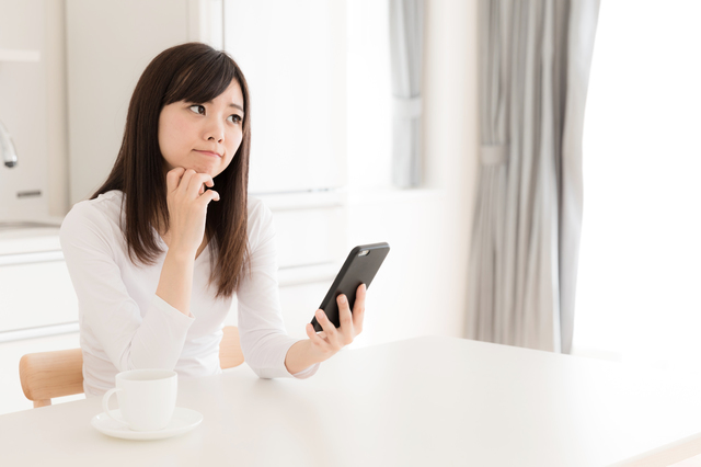 携帯を持って悩む女性,